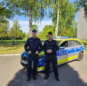 Dwaj policjanci stoją na tle radiowozu.