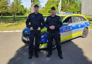 Dwaj policjanci stoją na tle samochodu.