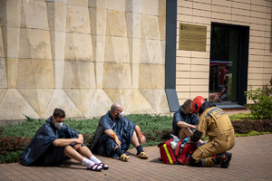 Ranni słuchacze siedzą na chodniku przy nich strażak pożarny.