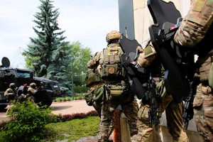 Policjanci kontrterroryści stoją przy budynki w gotowości.