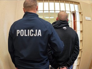 Policjant stoi tyłem obok zatrzymany stoi tyłem.
