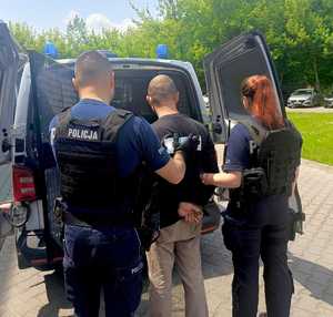 Policjantka i policjant wprowadzają zatrzymanego do radiowozu.