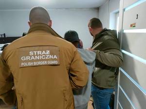 Funkcjonariusz Straży Granicznej i policjant prowadzą zatrzymanego.