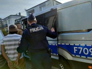 Funkcjonariusz Straży Granicznej i policjant prowadzą zatrzymanego do radiowozu.