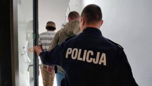 Policjanci prowadzą zatrzymanego po schodach.