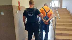 Policjant prowadzi po schodach zatrzymanego.