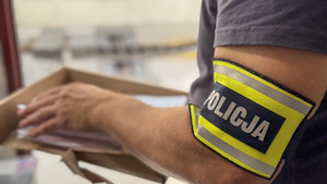 Reka policjanta z opaską  z napisem Policja, przegląda dokumenty.