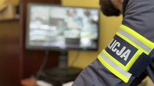 w tle monitor, ręka policjanta z opaska z napisem Policja.