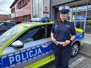 Policjantka ruchu drogowego stoi przy radiowozie w tle budynek.
