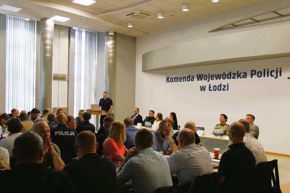 Na auli szkolenie, przy mównicy przemawia komendant, zaproszeni goście siedzą za stołami, i policjanci.