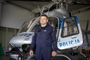 pilot policyjnego Bella, w tle policyjny śmigłowiec.