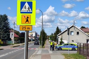 droga, znak drogowy z Agatką, w oddali radiowóz i policjanci ruchu drogowego.