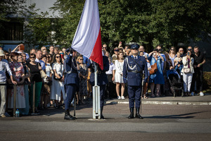 Poczet flagowy wciąga flagę na maszt, za nimi zebrane rodziny policjantów.