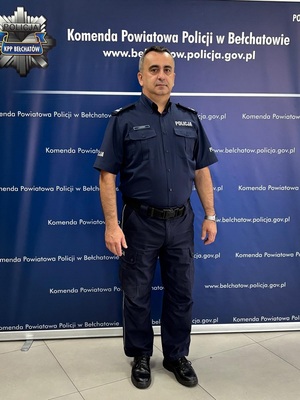 Policjant stoi na ściance granatowej.