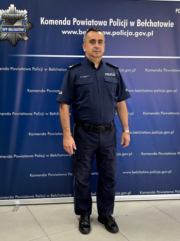 Policjant stoi na ściance granatowej.