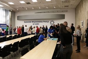 Grupa policjantów i pracowników cywilnych stoi w kolejce do badania.
