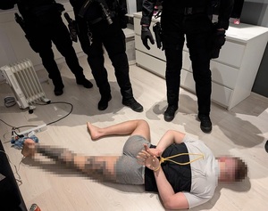 Mężczyzna z założonymi na ręce kajdankami leży na podłodze obok stroją kontrterroryści.