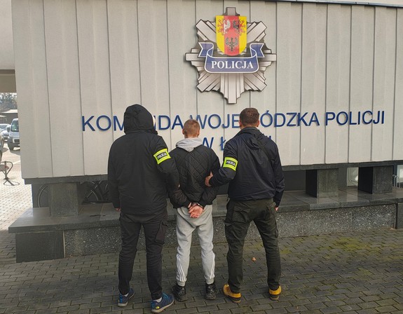 Policjanci stoją z zatrzymanym mężczyzną.