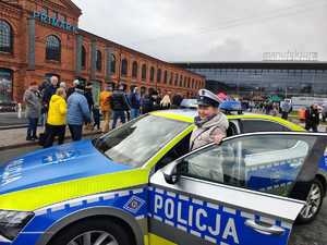 Radiowóz policyjny przy nim kobieta w czapce policyjnej.