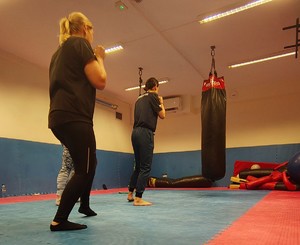 Instruktor prowadzi zajęcia na macie, biorą udział w nich kobiety.