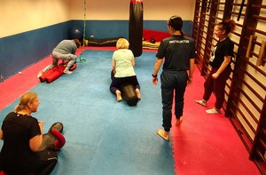 Instruktor prowadzi zajęcia na macie, biorą udział w nich kobiety.