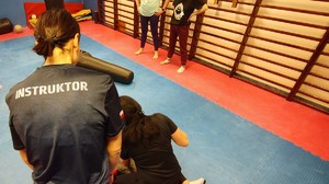 Instruktor prowadzi zajęcia na macie, biorą udział w nich kobiety.