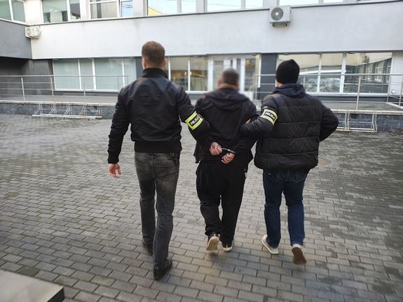 Policjanci prowadzą zatrzymanego mężczyznę.