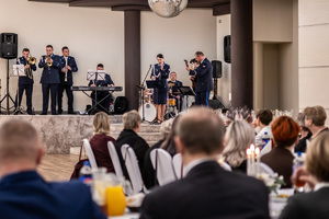 Orkiestra gra, publiczność siedzi na krzesłach.