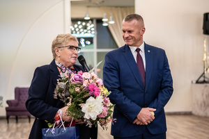 Komendant Wojewódzki Policji w  łodzi stoi obok kobiety która trzyma kwiaty.