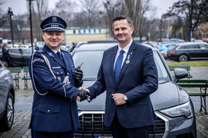 Policjant podaje rękę mężczyźnie z tyłu radiowóz.