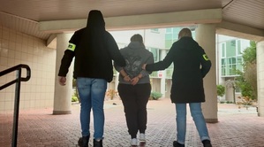 Policjanci prowadzą osobę zatrzymaną.