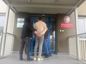 Policjanci prowadzą osobę zatrzymaną.