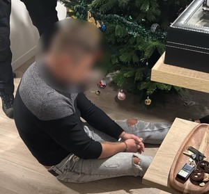 Zatrzymany siedzi na podłodze, ma skute ręce w kajdanki.