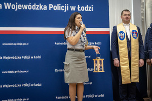 Przemawia kobieta w stroi harcerki obok stoi ksiądz.