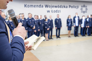 Policjanci w mundurach i zaproszeni goście. Na pierwszym planie policjant z mikrofonem.