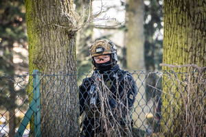 Policjant z bronią obserwuje zza ogrodzenia.