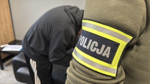 Napis policja, w tle zatrzymany mężczyzna.