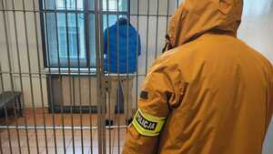 Policjant z opaską policja, za kratami zatrzymany.