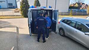 Policjant z zatrzymanym przy radiowozie.