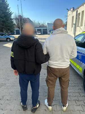 Policjant z zatrzymanym przy radiowozie.