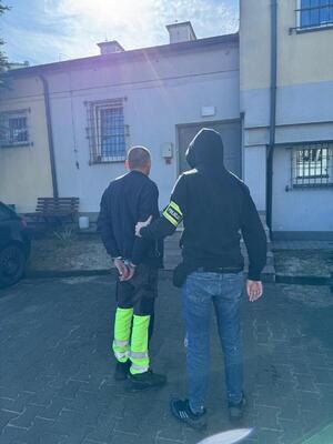Policjant z zatrzymanym przed budynkiem.