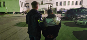 Policjant z zatrzymanym przed budynkiem wokół samochody w tym radiowóz.