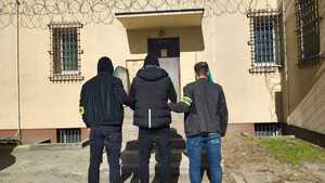Dwaj policjanci z zatrzymanym przed budynkiem.