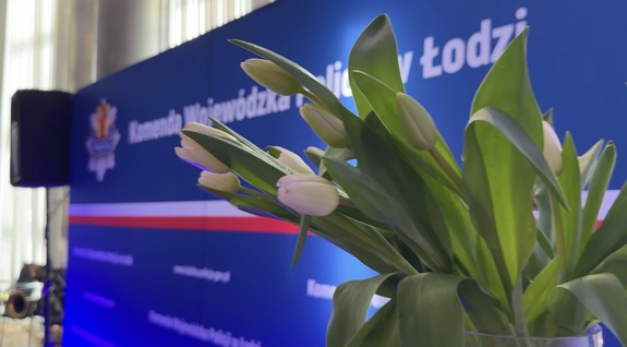 Napis Komenda Wojewódzka Policji w Łodzi, w tle kwiaty.