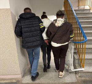 Policjanci prowadzą zatrzymaną kobietę.
