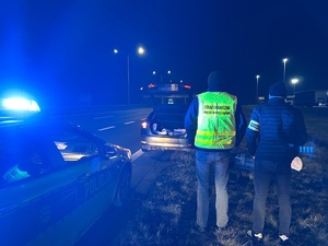 Policjant i strażnik graniczny stoją przy samochodach.