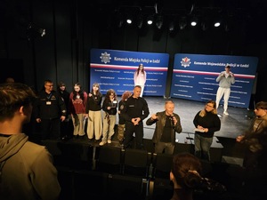 Uczestnicy wydarzenia stoją na scenie oraz przed sceną wraz z zaproszonymi gośćmi.