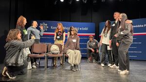 Uczestnicy wydarzenia siedzący lub stojący na scenie podczas prób.