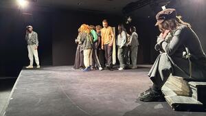 Uczestnicy stojący i siedzący na scenie podczas przedstawienia.