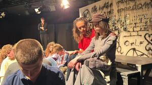 Uczestnicy wydarzenia stojący i siedzący na scenie.